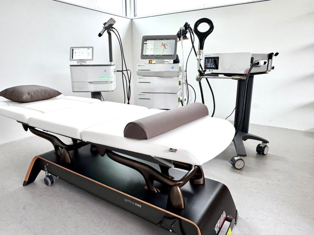 Behandlungsraum mit Stoßwelle-Geräten und Liege in einer Sportmedizinischen Praxis in Wien